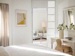 Ein Hotelzimmer mit Bett, Schreibtisch, Stuhl, Lampe, Blumen in einer Vase und einem Spiegel.