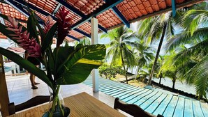 A wooden table with a potted plant, a covered outdoor area with a pool, and palm trees. - Playa Mango (Bocas del Toro)