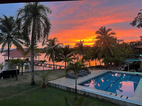 Ein Poolbereich mit Sonnenuntergangsblick, Palmen und einer Holzterrasse.