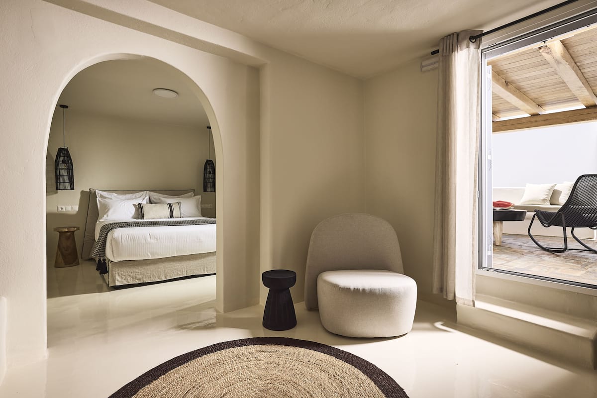 A bedroom with a bed, a chair, a small table, and a view through a window.