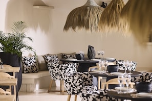 A modern dining area with black and white patterned furniture, a large potted plant, and hanging light fixtures.