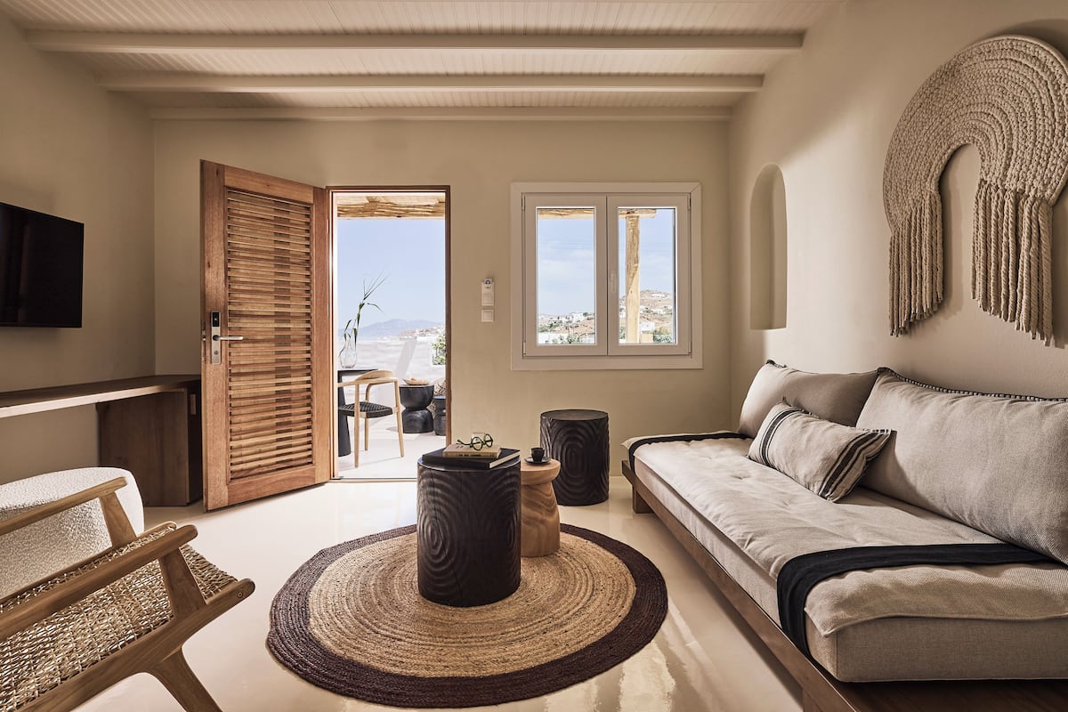 A modern living room with a sofa, a wooden chair, a coffee table, and a TV mounted on the wall.