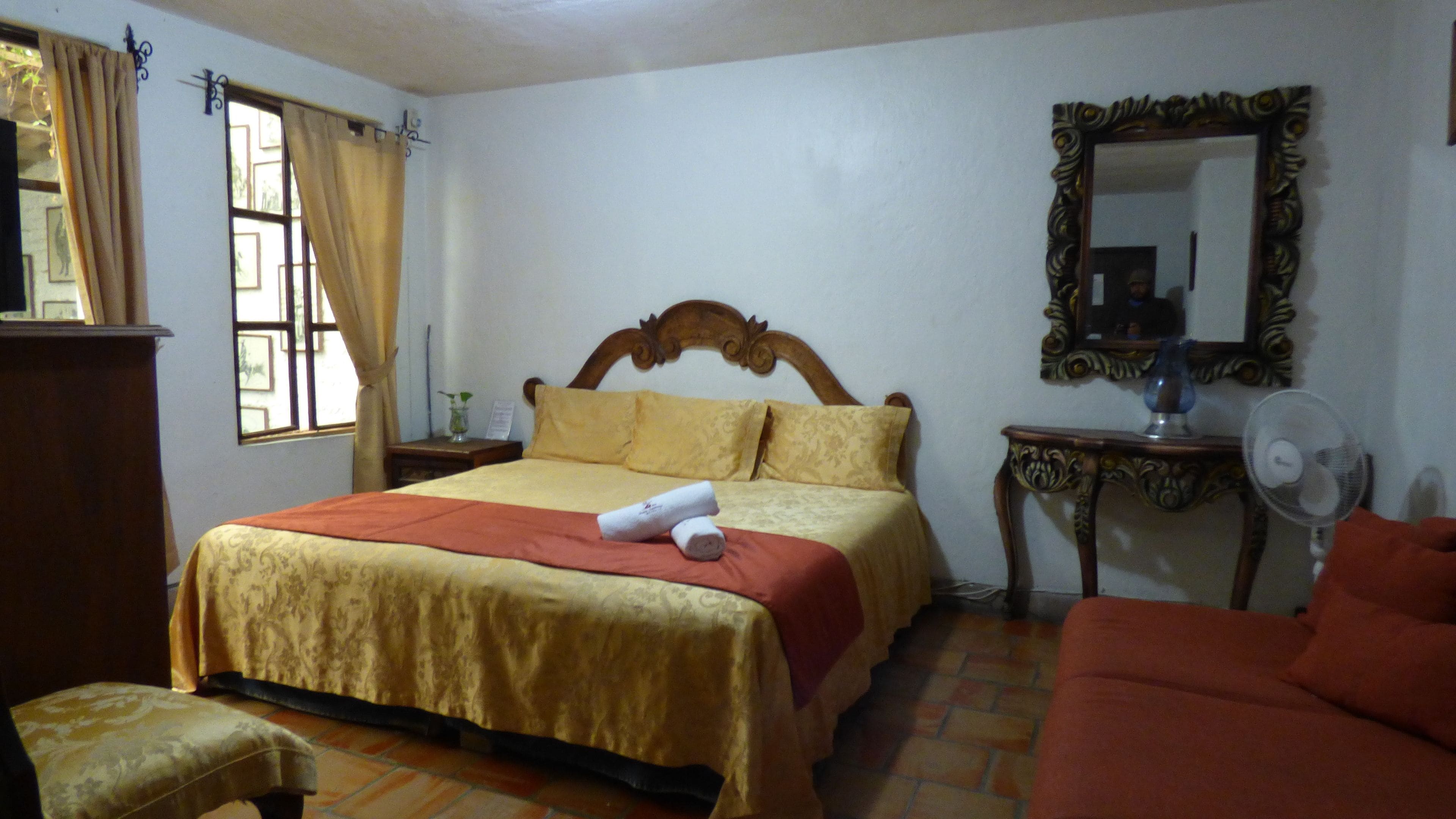 Una habitación de hotel con cama, mesita de noche, espejo, silla y ventana con cortinas.