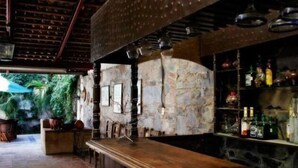 A bar area with a stone wall, wooden bar counter, and shelves with bottles. - Hotel Santo Santiago (Tonalá)