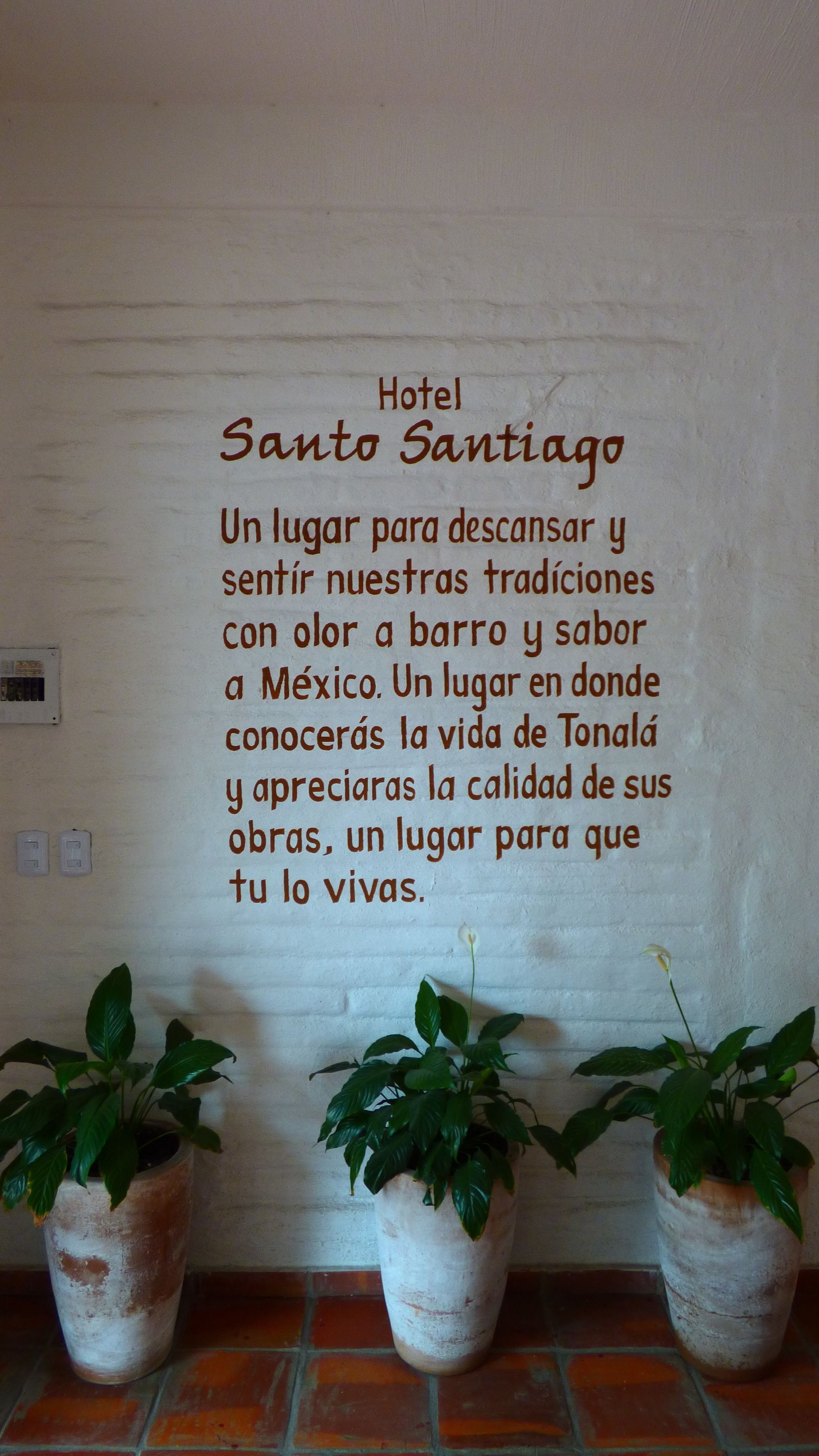 A wall with a sign for Hotel Santo Santiago, describing it as a place to relax and enjoy traditions with a bar and Mexican flavors.