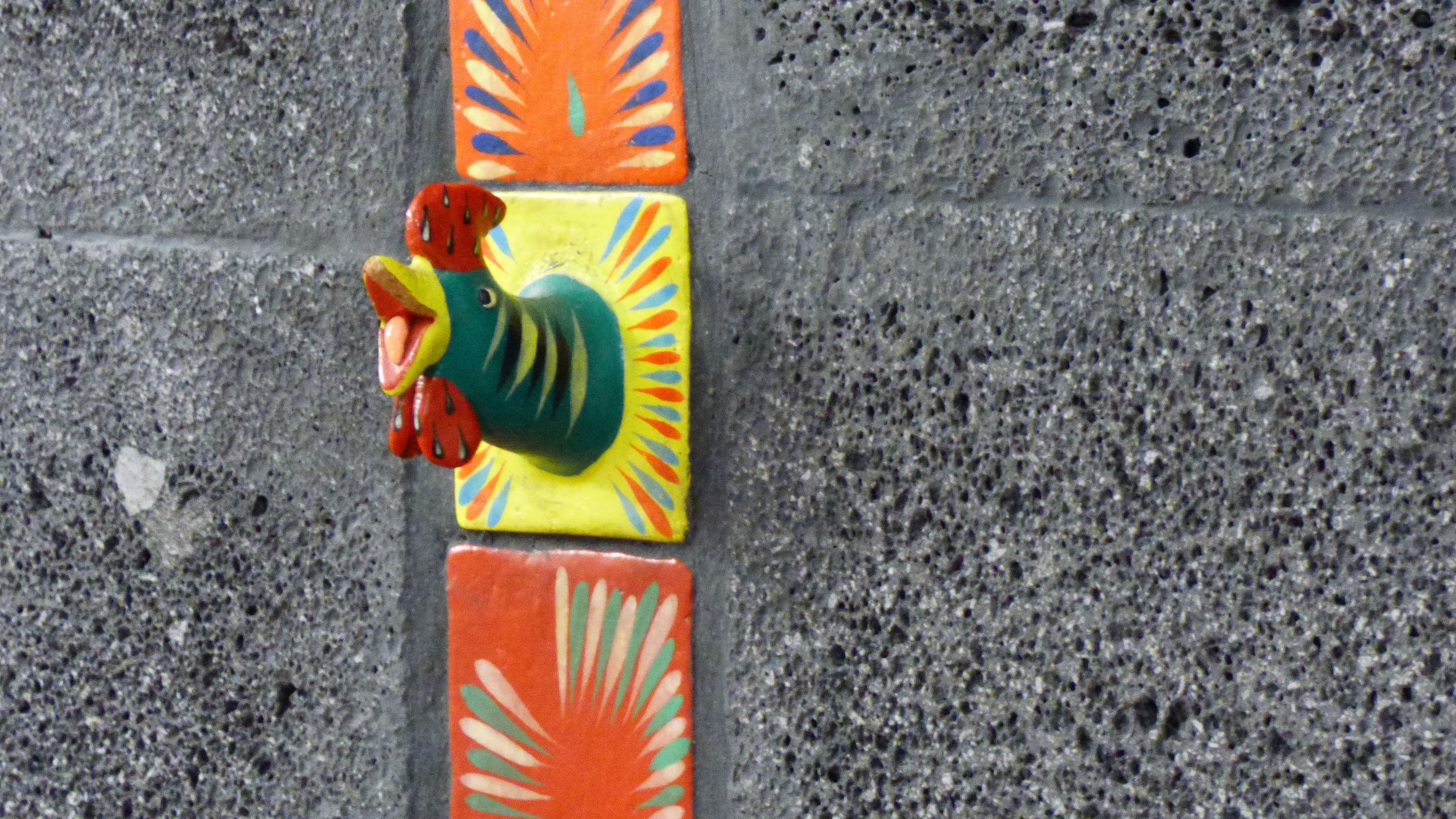 Un hidrante con forma de pájaro, de color vibrante, sobre una superficie de concreto texturizado.
