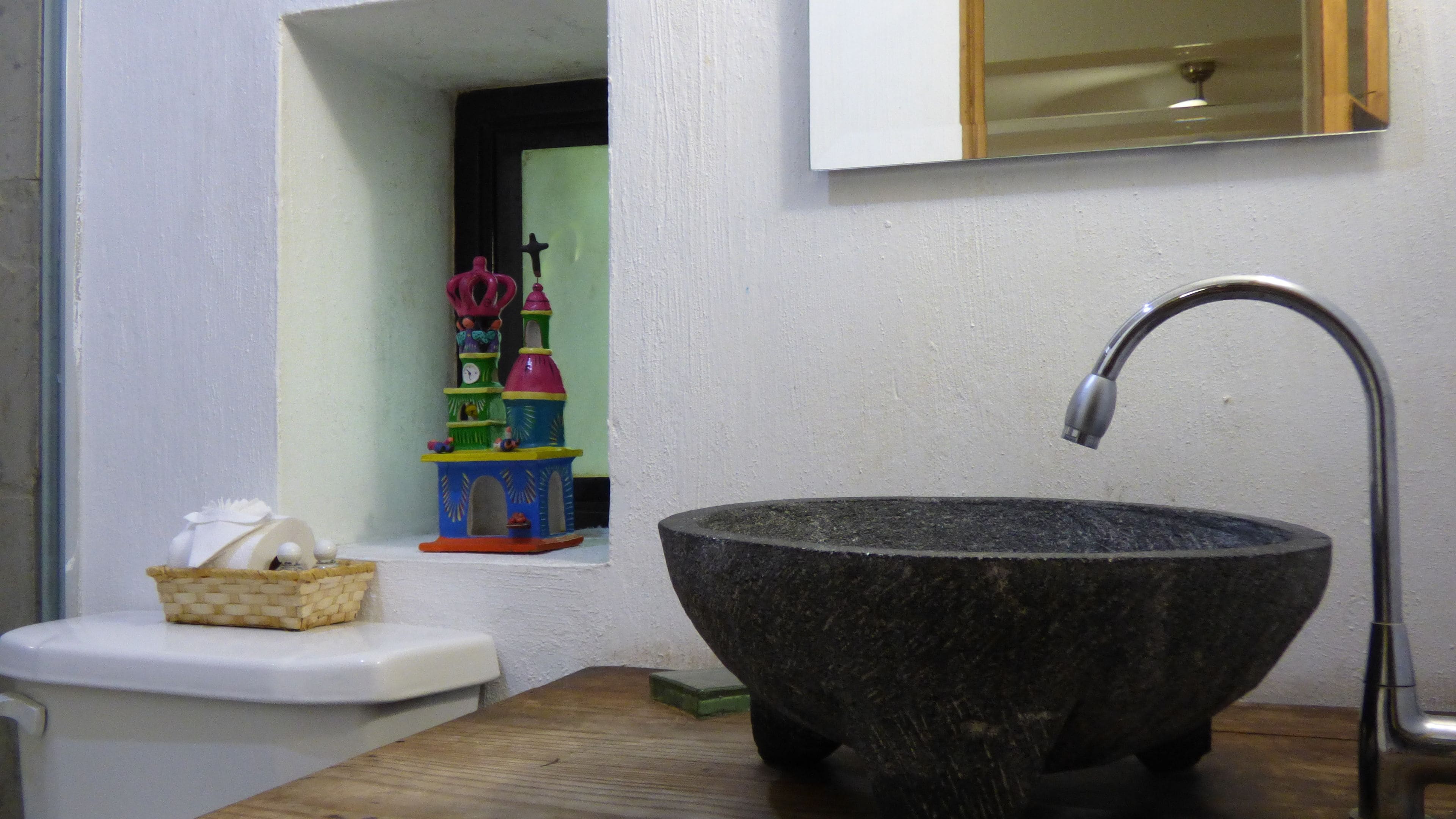 Une salle de bain avec un grand lavabo en pierre, des toilettes et une petite étagère sur laquelle se trouve un panier.
