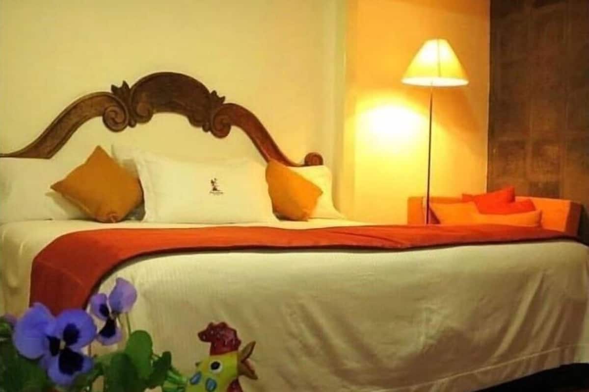 A bedroom with a wooden headboard, a bed with white bedding and orange pillows, a floor lamp, and a wall-mounted artwork.