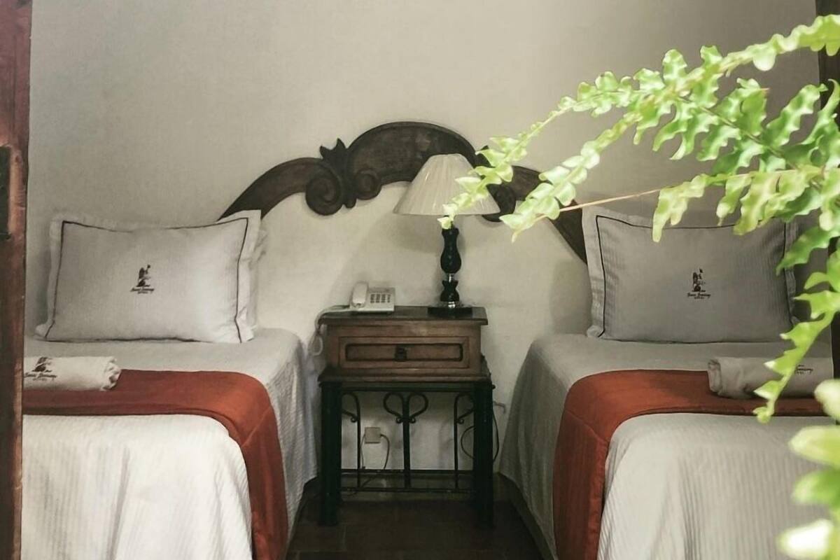 A room with two beds, a nightstand with a lamp, and a decorative headboard.