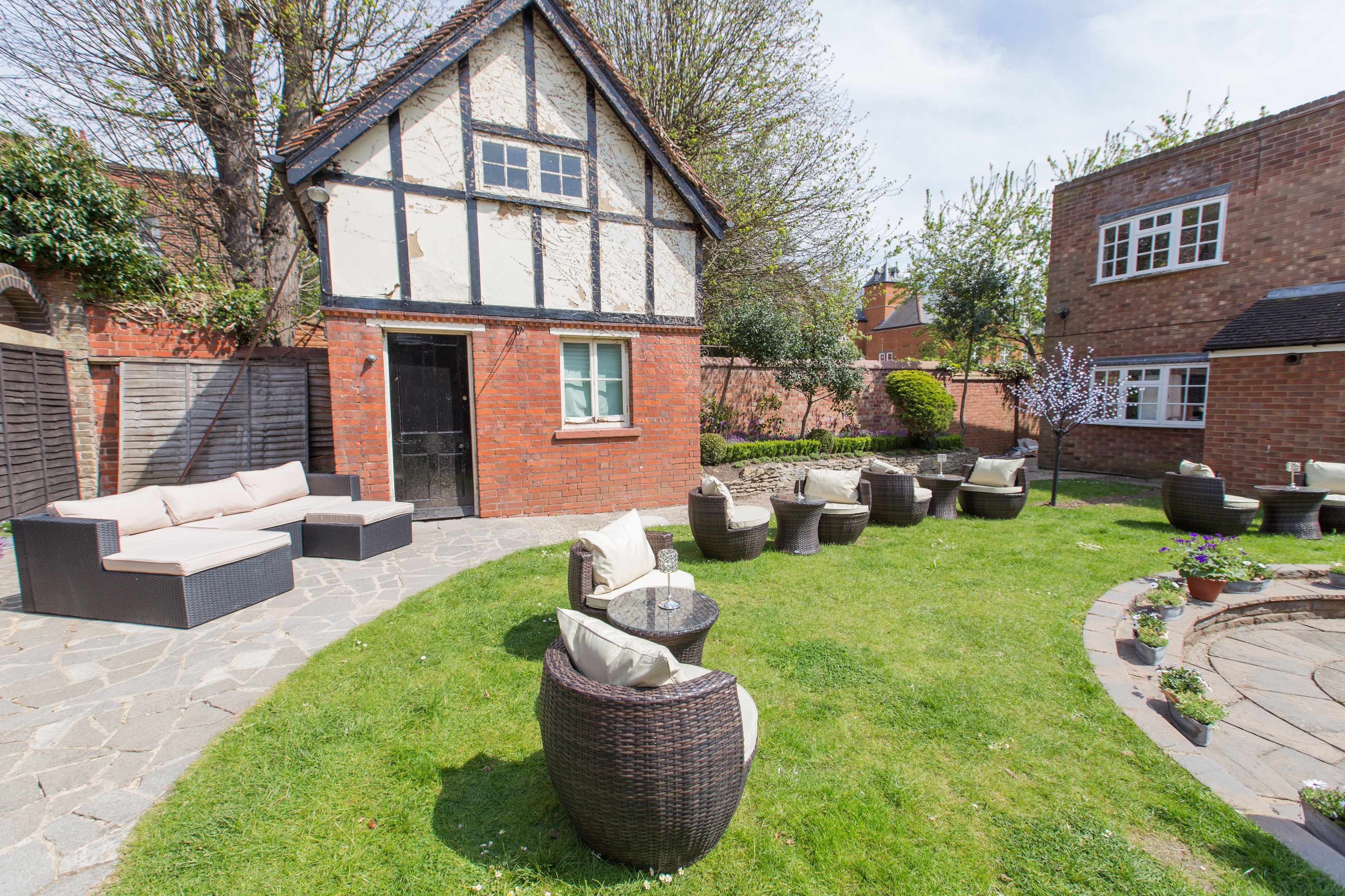 A courtyard with outdoor furniture, a house with exposed brick and timber framing, and a garden with potted plants.