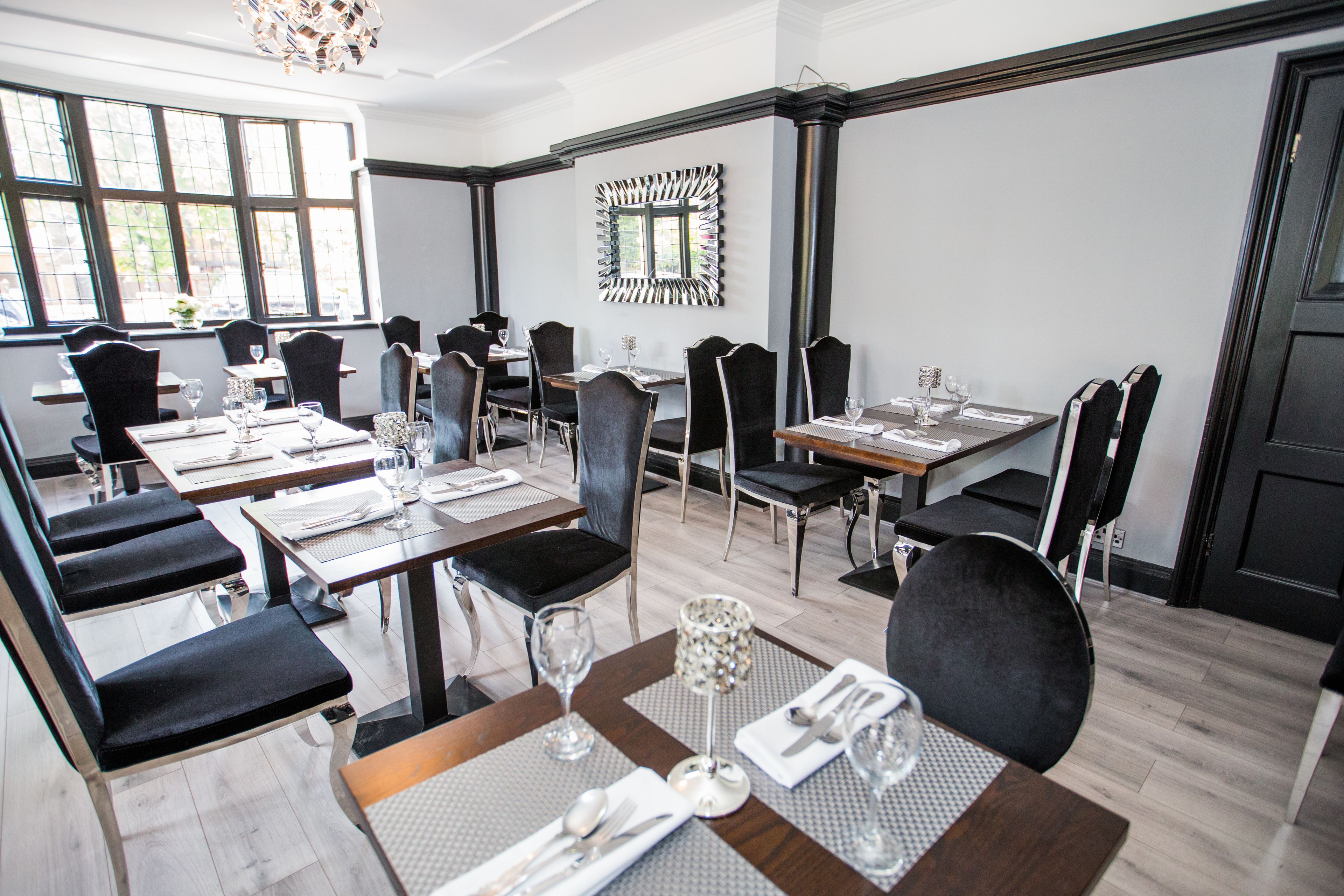 A dining area with multiple tables and chairs, arranged in a modern setting with a large window providing natural light.