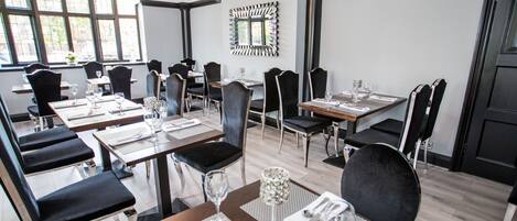 A dining area with multiple tables and chairs, arranged in a modern setting with a large window providing natural light.
