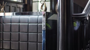 Una panca imbottita nera con un piano in vetro, una balaustra nera e un'ampia colonna nera.