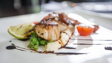 A plate of food with seared scallops, a slice of tomato, and a lime wedge.