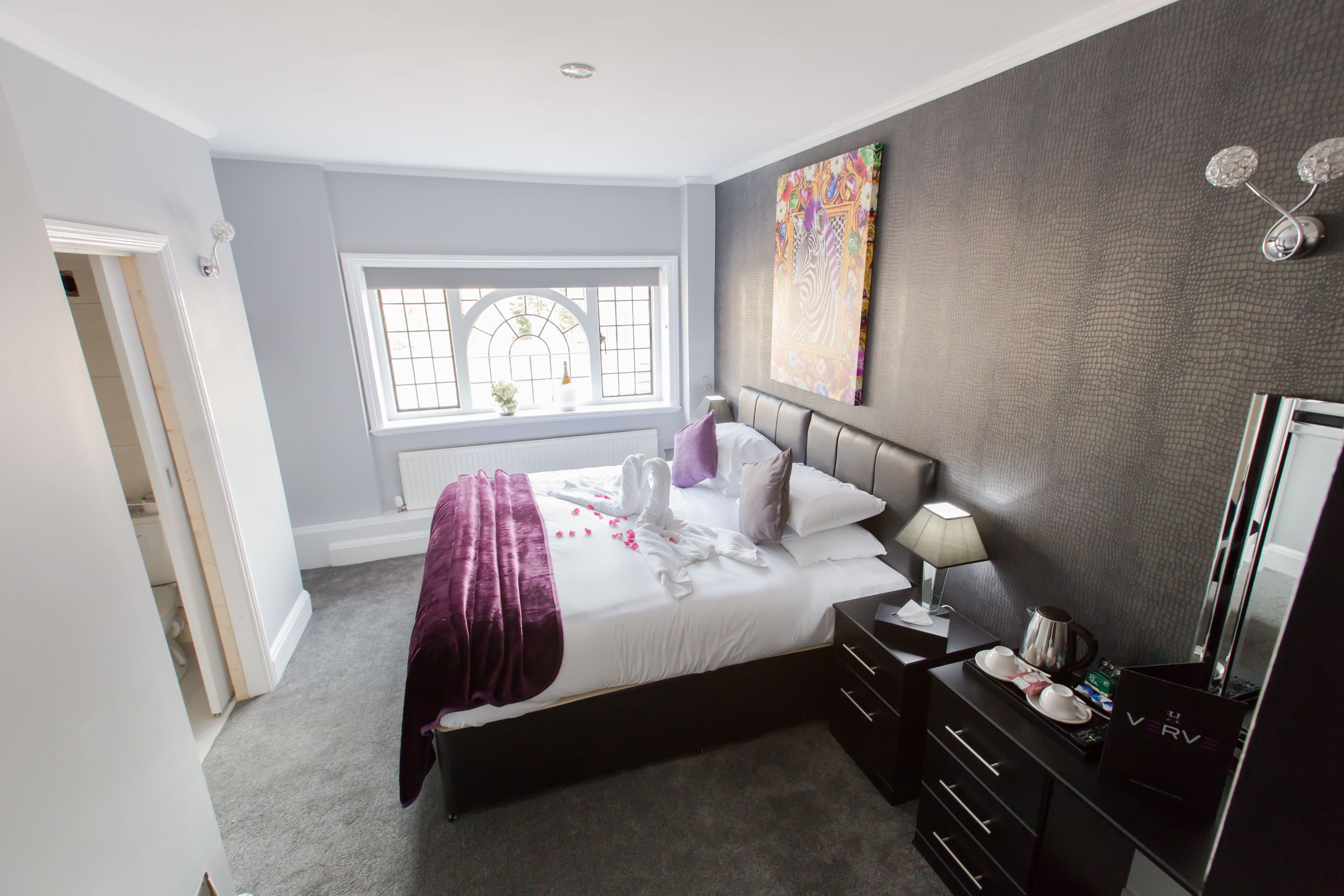 A modern bedroom with a large bed, a dresser, a vanity, and a window with a view.