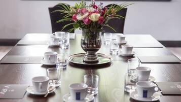 Una mesa de comedor dispuesta con tazas y platillos blancos, una copa de cristal transparente y un florero con flores.