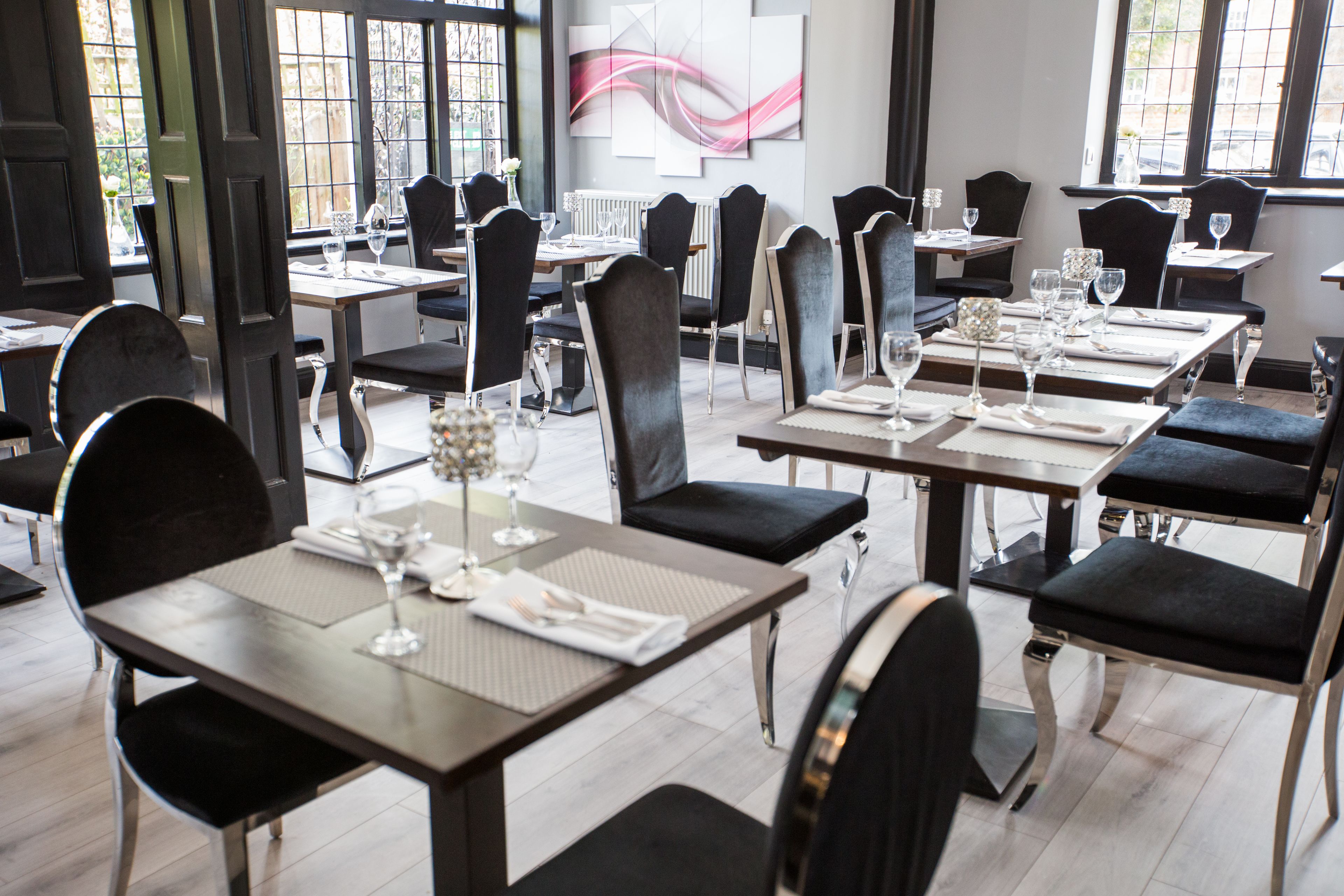 A restaurant with multiple tables and chairs, each set with wine glasses and cutlery.