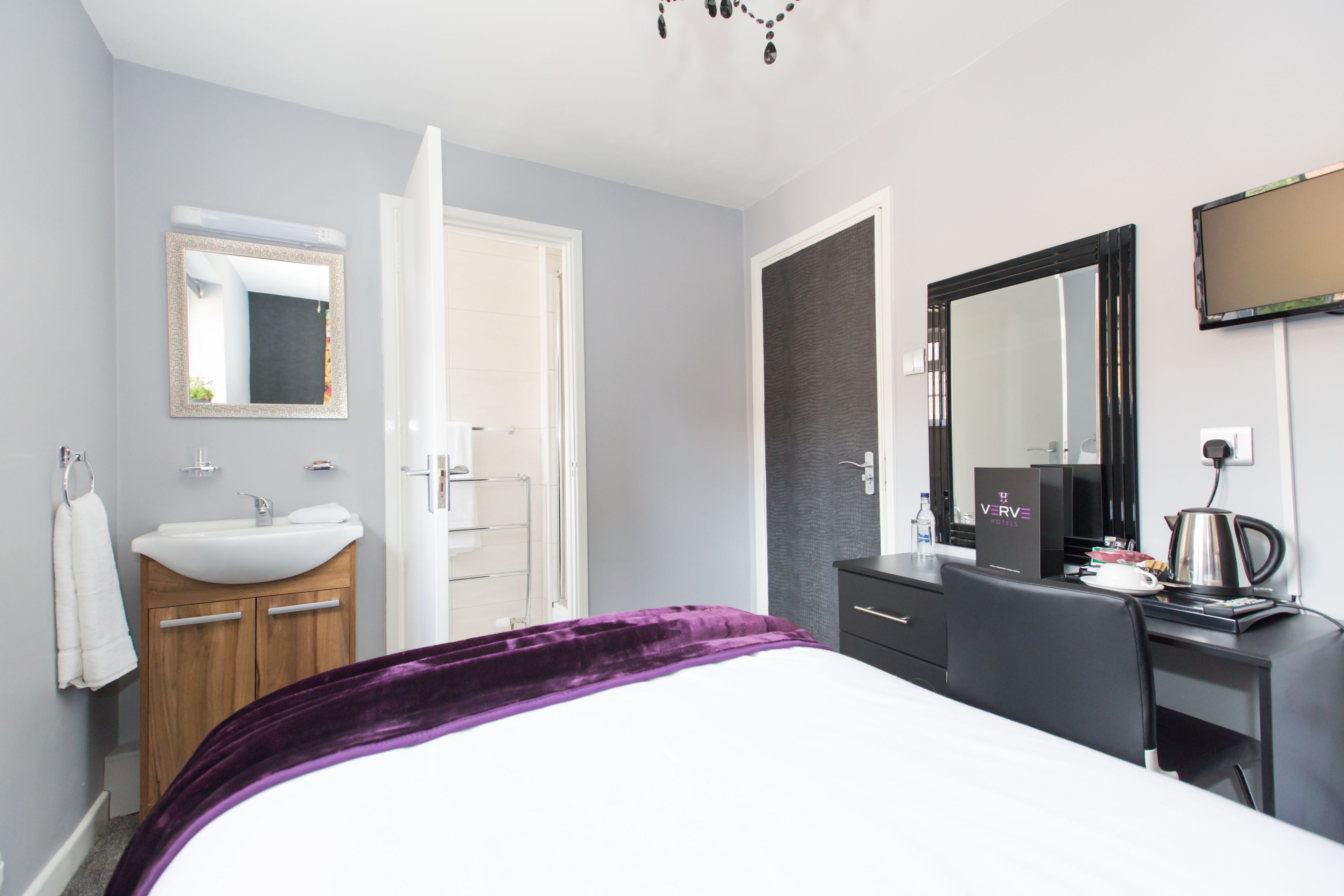 Habitación de hotel con cama, escritorio, espejo, lavamanos y ducha.