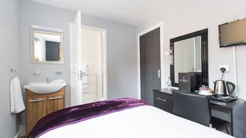 Habitación de hotel con cama, escritorio, espejo, lavamanos y ducha.