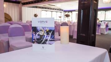 Un folleto de boda sobre una mesa con una vela, en una habitación con sillas y mesas blancas, y un candelabro.