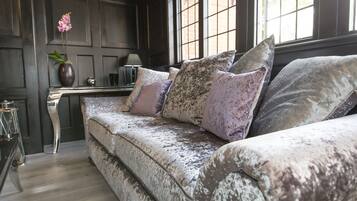 A dark wood-paneled room with a plush sofa, a vase with flowers, and a lamp on a side table.