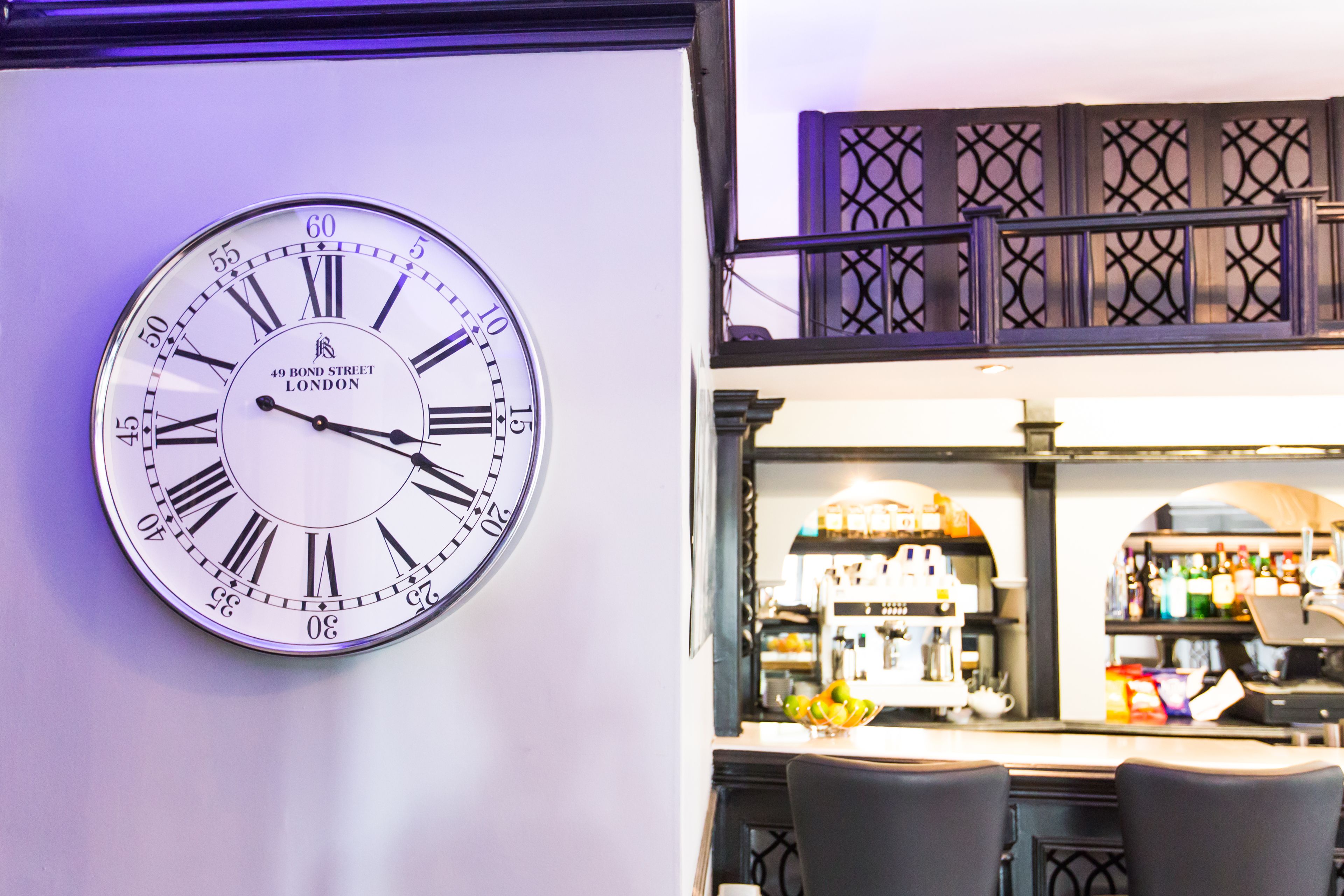Un reloj de pared con números romanos y la inscripción '49 Bond Street London' sobre una pared blanca.
