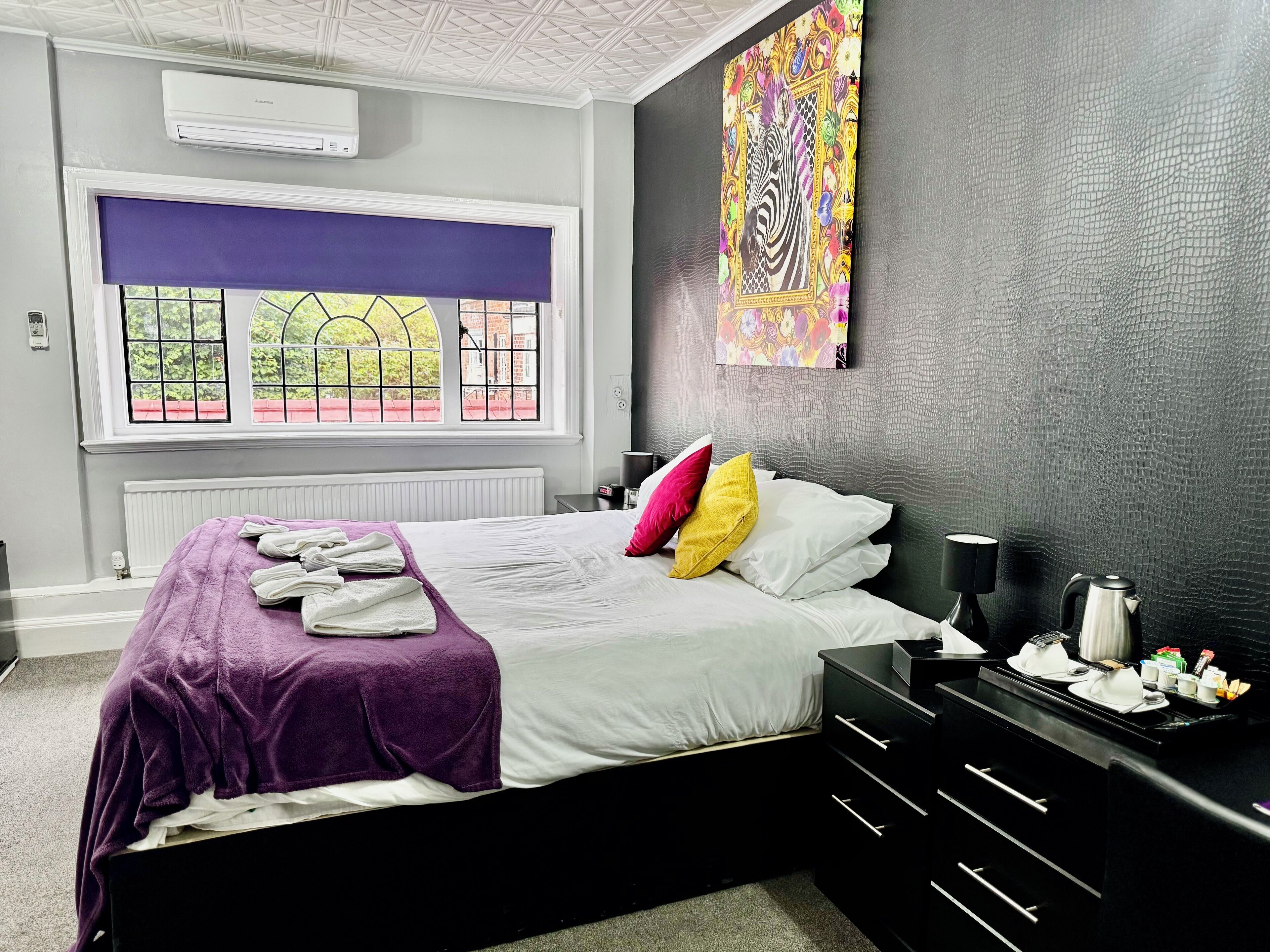 Un dormitorio con una cama grande, una ventana con vistas, un aparador negro y un aire acondicionado de pared.