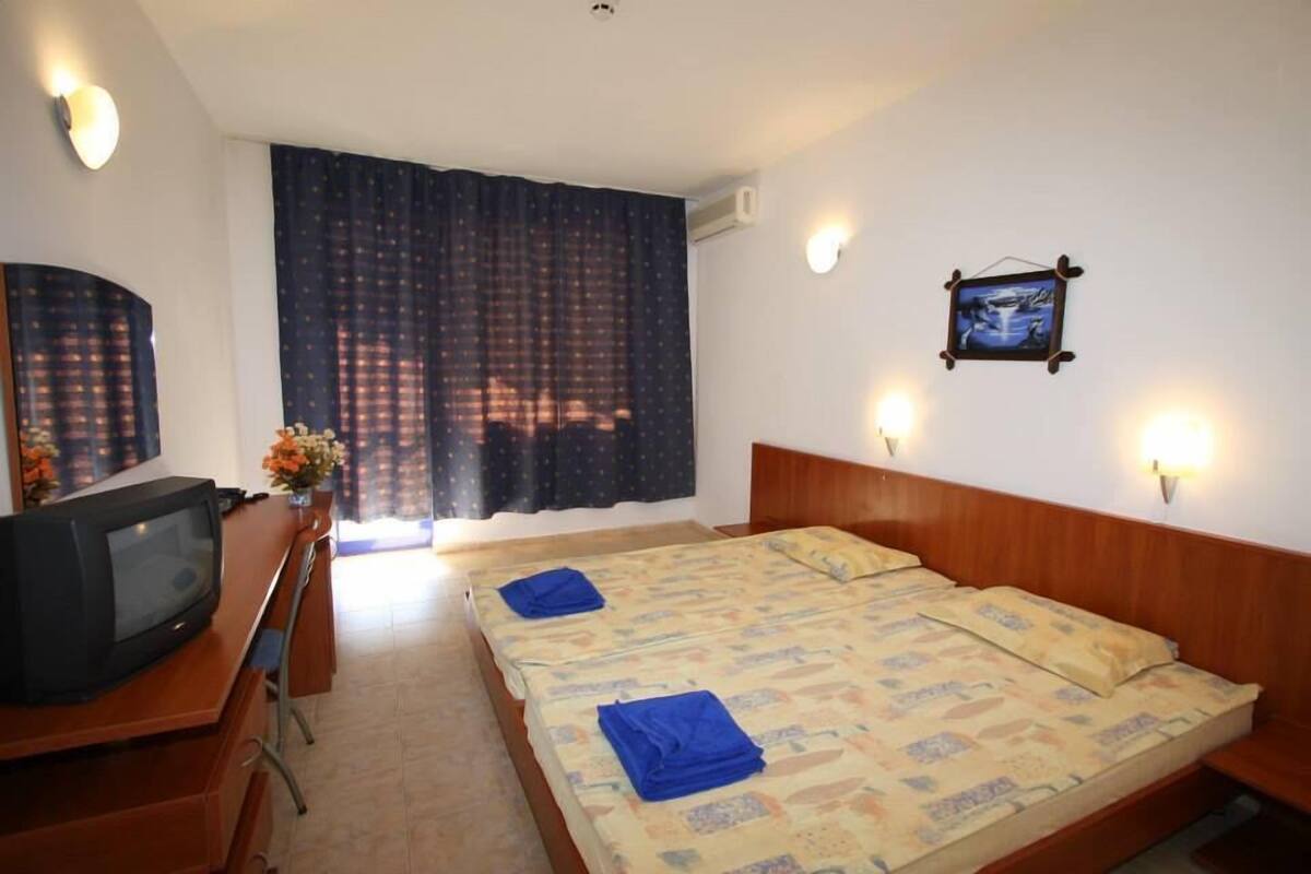 A hotel room with a bed, a desk with a television, and two wall-mounted lights.