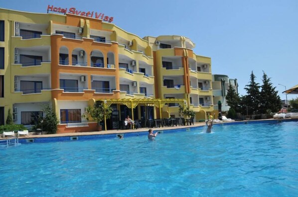 A hotel with a swimming pool, multiple balconies, and outdoor seating areas.