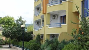 A multi-story building with balconies, air conditioning units, and a paved walkway with greenery. - Sveti Vlas Hotel (Sveti Vlas)