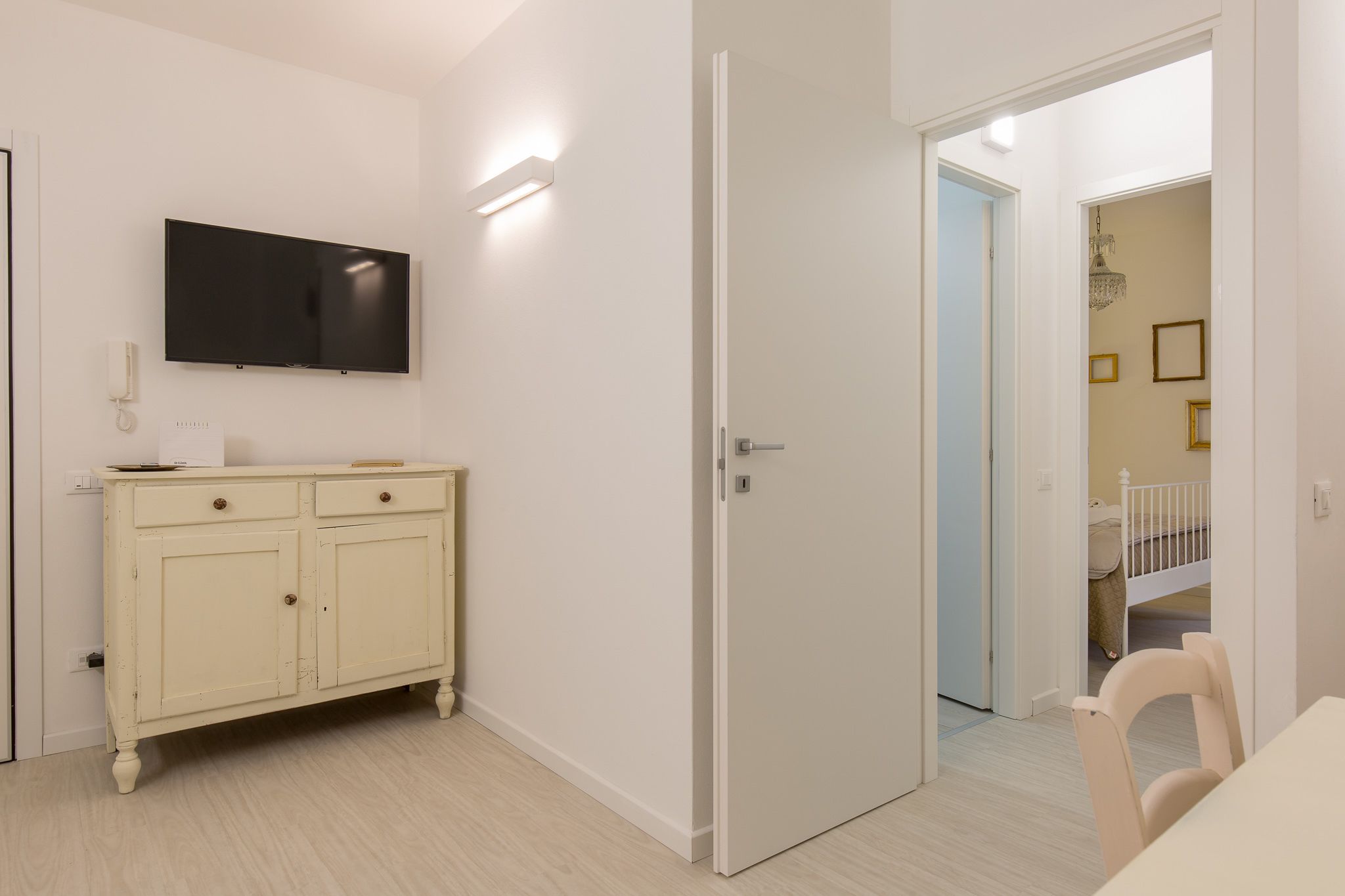 A room with a white cabinet, a flat-screen TV mounted on the wall, and a door leading to another room.