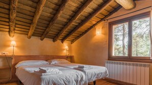 A cozy bedroom with a wooden ceiling, a large window with a view of trees, and two bedside lamps.