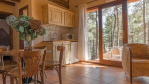 A cozy kitchen with wooden cabinets, a dining table with chairs, and a view of a forest through large sliding glass doors.