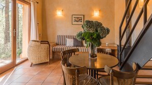 A cozy room with a round dining table, wicker furniture, and a large window offering a view of trees.