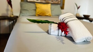 A neatly made bed with a striped towel and a red flower, a yellow pillow, and a decorative headboard.