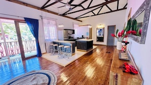 A spacious living area with a wooden floor, a kitchen with a central island, and a balcony with a view.