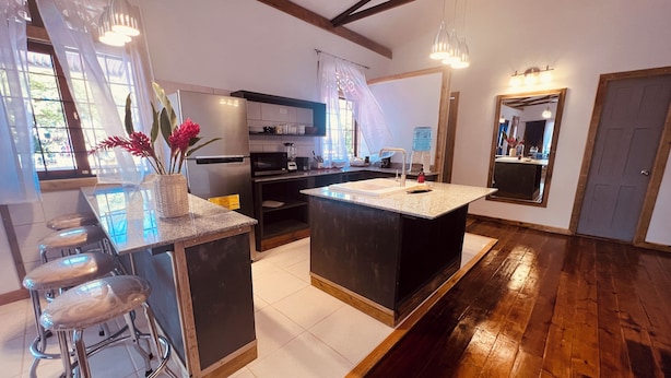 A modern kitchen with a central island, bar stools, a microwave, and a sink.