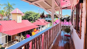 A covered outdoor area with a wooden deck, red awnings, and a view of the surrounding buildings and palm trees.
