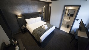 Quarto de hotel com uma cama grande, mesa de cabeceira com telefone, espelho e pequena escrivaninha com cadeira.
