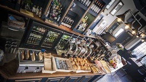 Uma área de bar com diversos tipos de garrafas, uma geladeira e uma vitrine de pães.