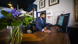Um homem trabalhando em uma mesa de madeira com um monitor de computador, rodeado por quadros nas paredes.