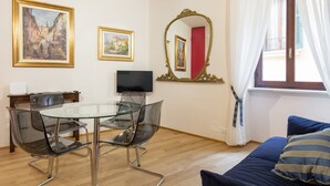 A room with a glass dining table, clear chairs, a flat-screen TV, a bed with blue bedding, and two framed paintings on the wall. - Casa Sottoriva (Verona)