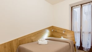 A bedroom with a wooden headboard, a bed with beige bedding, a white towel on the bed, and sheer curtains on the window. - Casa Sottoriva (Verona)