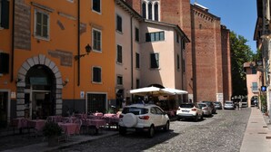 A cobblestone street with parked cars and outdoor seating at a café. - Casa Sottoriva (Verona)