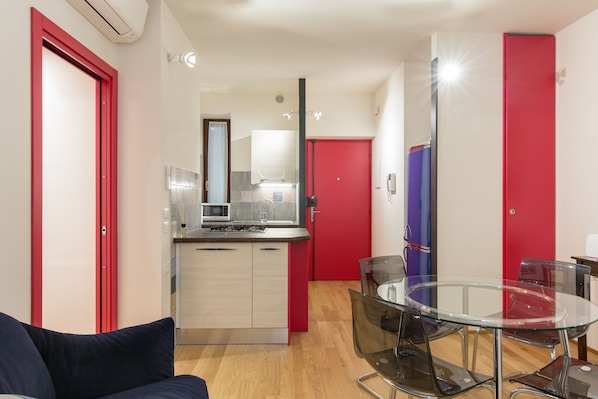 A modern kitchen with a microwave, a sink, and a red door. There is a glass table with chairs in the foreground.