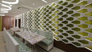 Un restaurant moderne avec des cloisons vertes hexagonales, des tables blanches et des bancs à motifs.