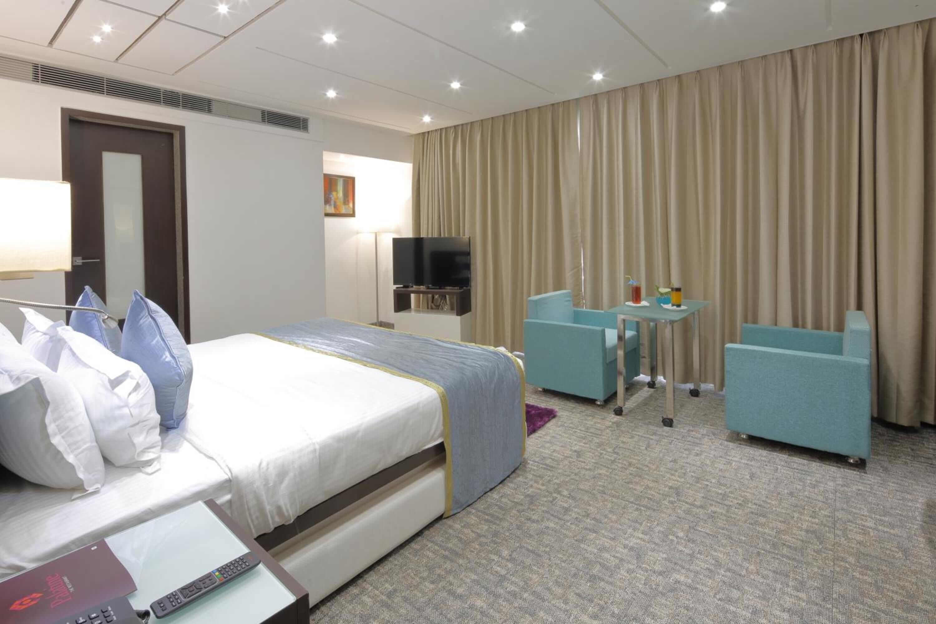 Une chambre d’hôtel avec un lit, une télévision, un bureau, deux chaises et un rideau.