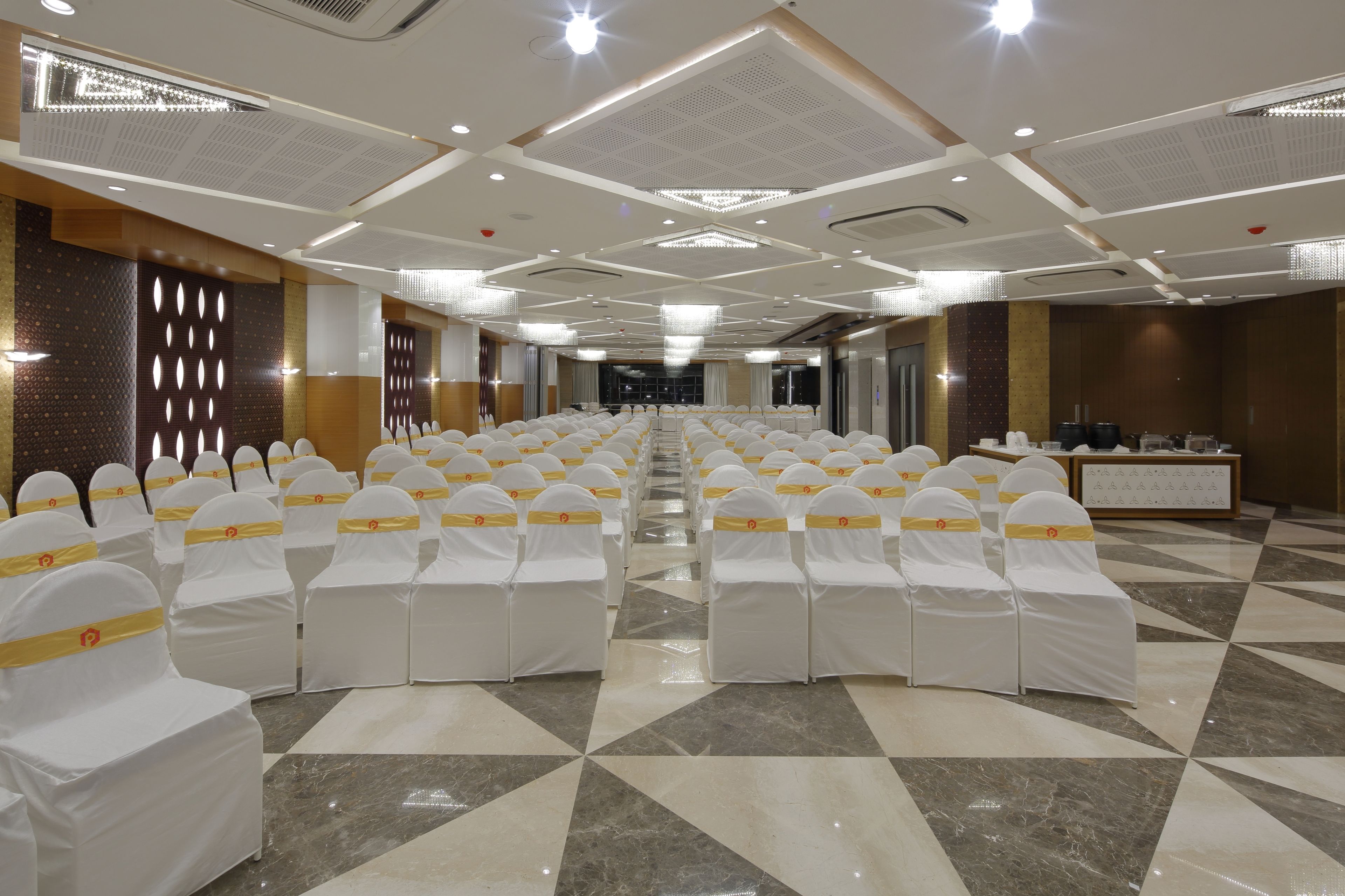 A conference room with rows of white chairs with yellow sashes, a polished marble floor, and a modern ceiling design.