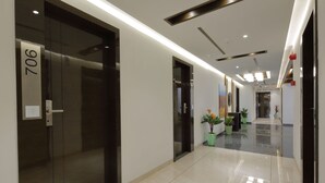 Un couloir d’hôtel moderne, avec un sol ciré, une porte portant l’inscription « 706 » et des plantes en pot disposées le long du mur.