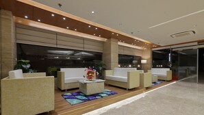 Un hall d’entrée moderne doté d’un espace salon avec des canapés et une table basse, d’une grande fenêtre avec des stores et d’un plancher en bois.